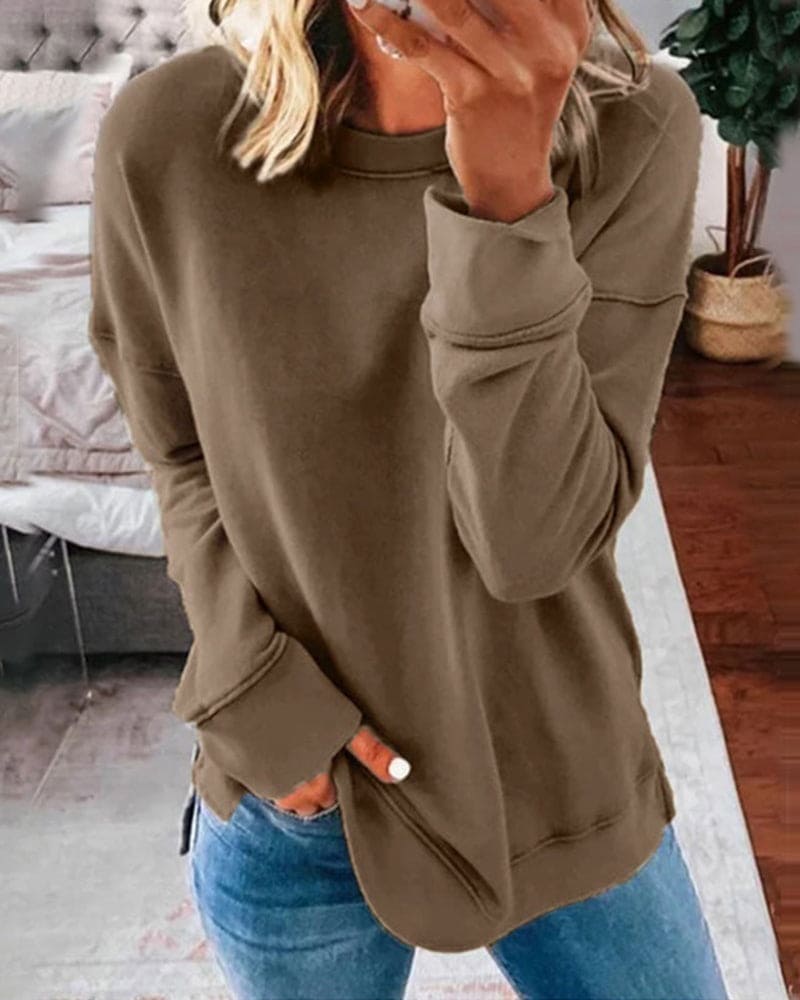 Person wearing a brown sweatshirt and blue jeans in a room with a couch and plant.