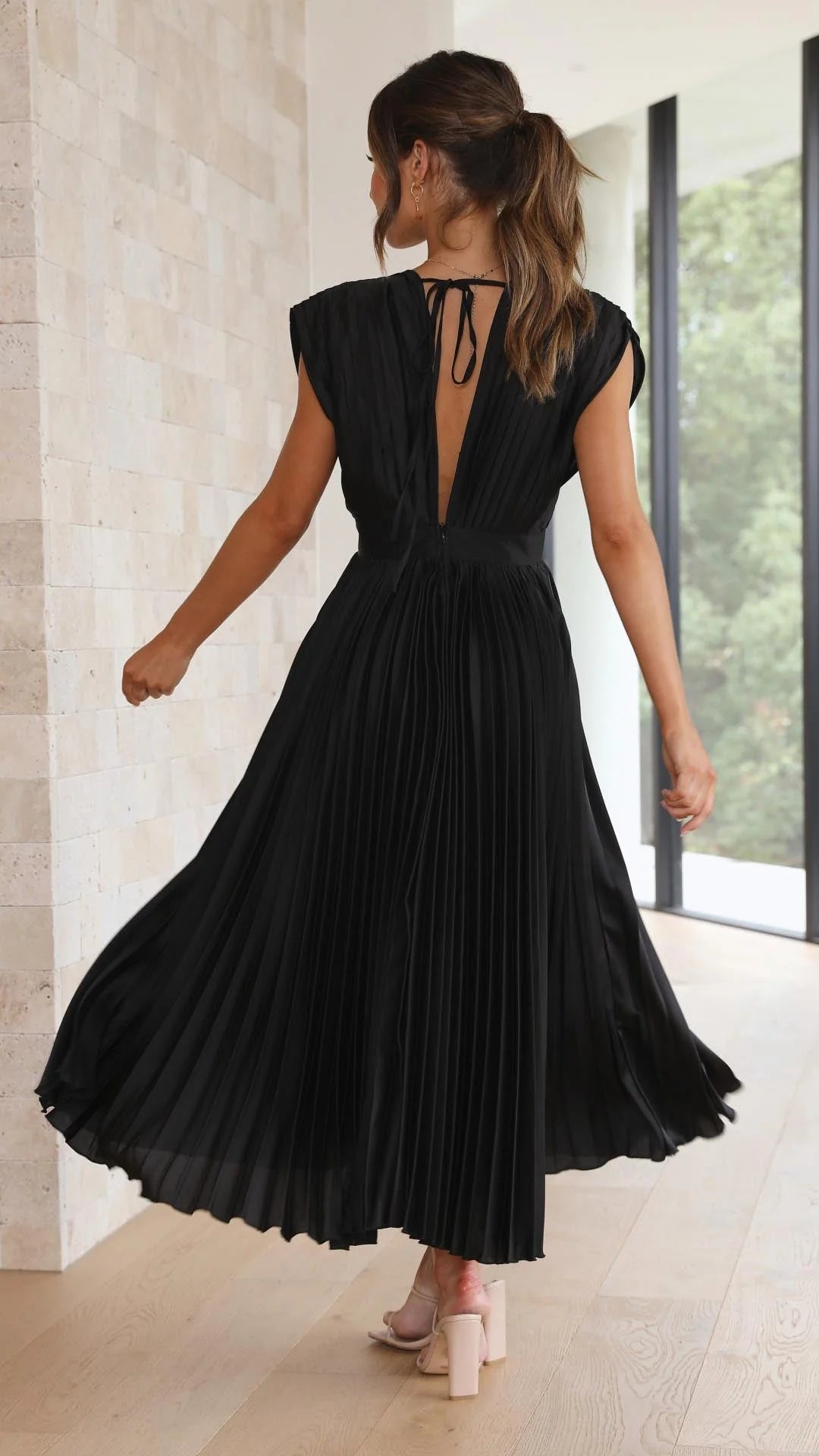Woman styling pleated maxi dress with delicate necklace and sandals