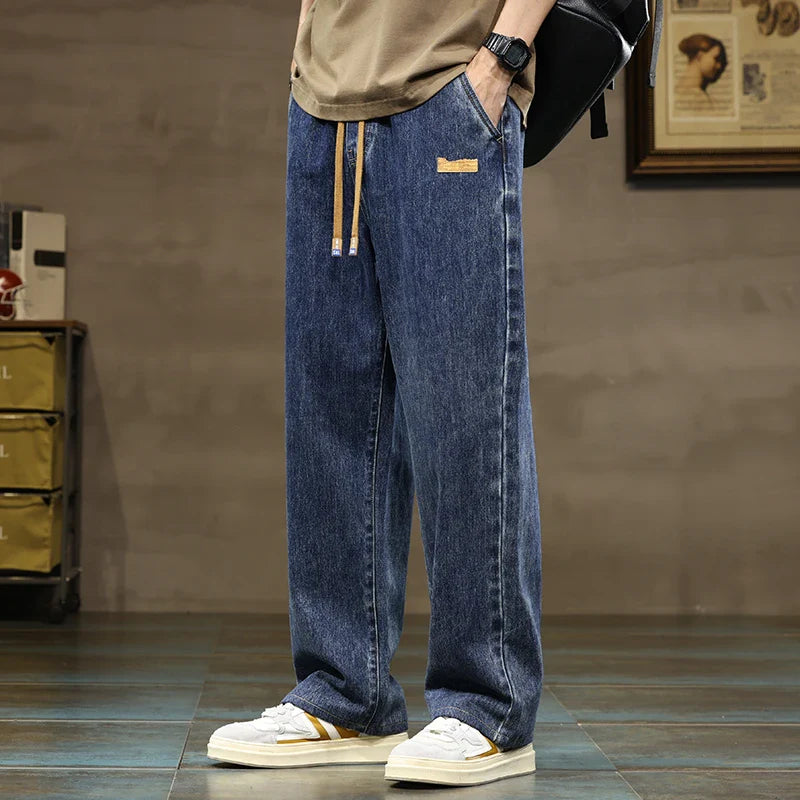 Men's relaxed fit wide leg jeans with drawstring waist in medium wash denim worn with tan sweatshirt