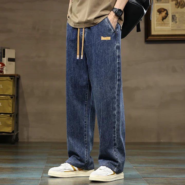 Men's relaxed fit wide leg jeans with drawstring waist in medium wash denim worn with tan sweatshirt