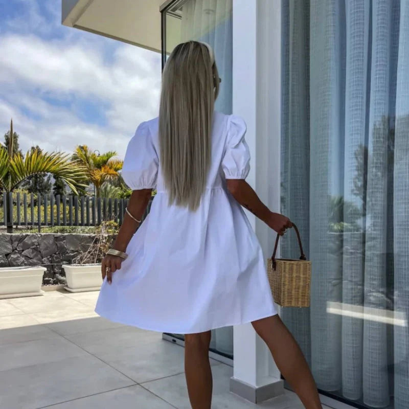 Flared mini dress with bow detail and puff sleeves styled with sandals and woven bag