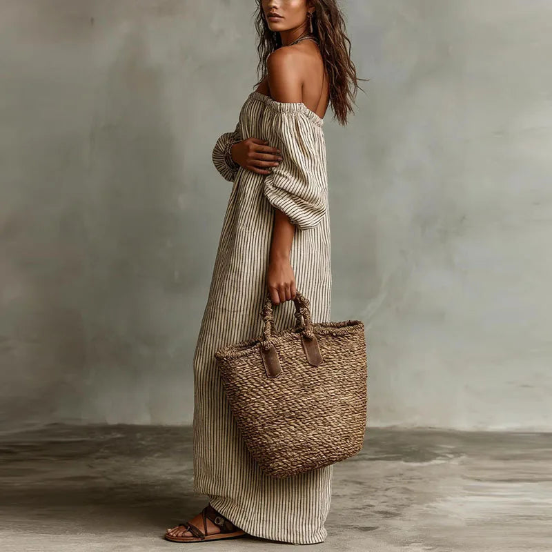 Model wearing striped off shoulder dress with woven bag and flat sandals