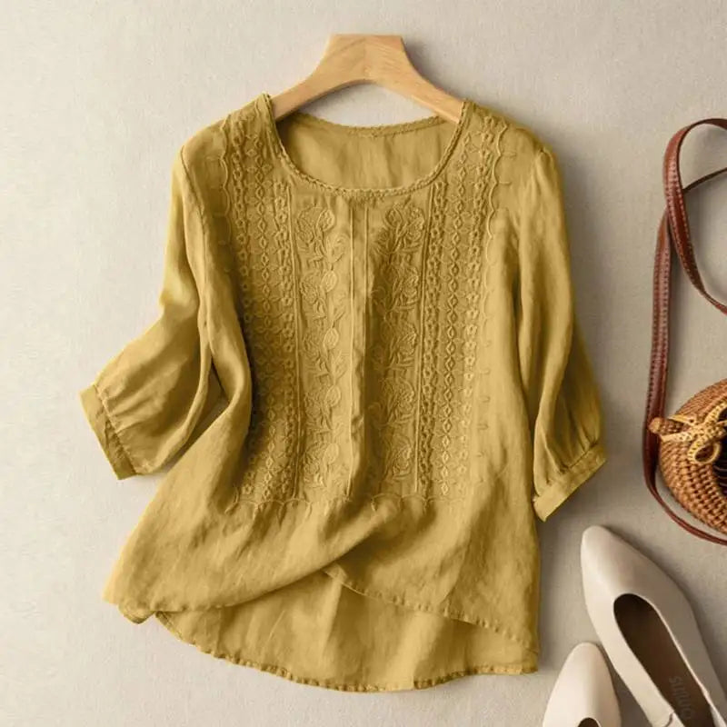 Women's linen blouse in mustard yellow with embroidered front panels and three-quarter sleeves displayed on hanger