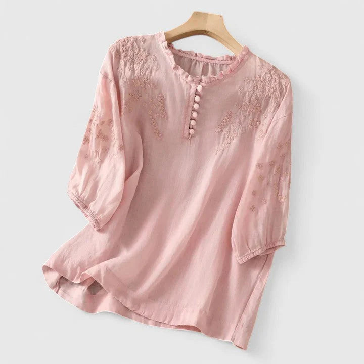 Women's embroidered button-front blouse in soft pink with lace detailing and three-quarter sleeves on wooden hanger