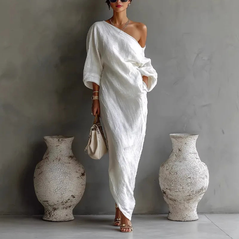 Woman wearing a white linen one shoulder dress with asymmetrical hem and batwing sleeves in a minimalist setting