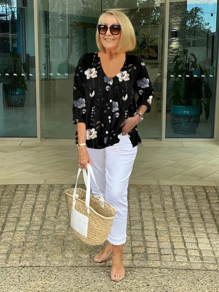 Women's floral print V-neck blouse styled with white trousers and sandals.