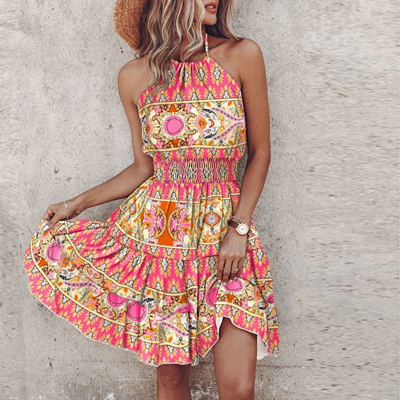 Woman wearing vibrant printed halter neck summer mini dress with smocked waist and open back design