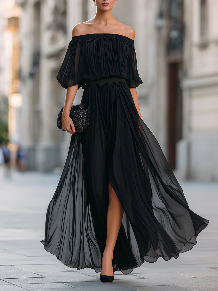 Woman wearing black off shoulder pleated maxi dress with flowing skirt and sheer sleeves for formal events